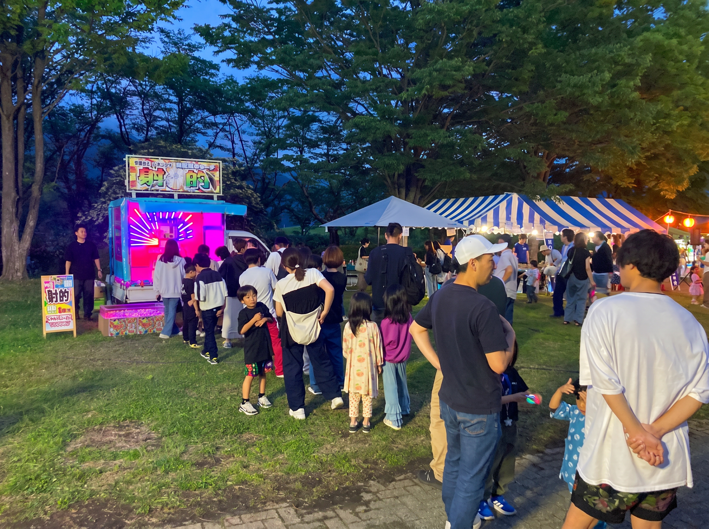 夜のイベントで射的に列をなす家族と子どもたちの集客風景